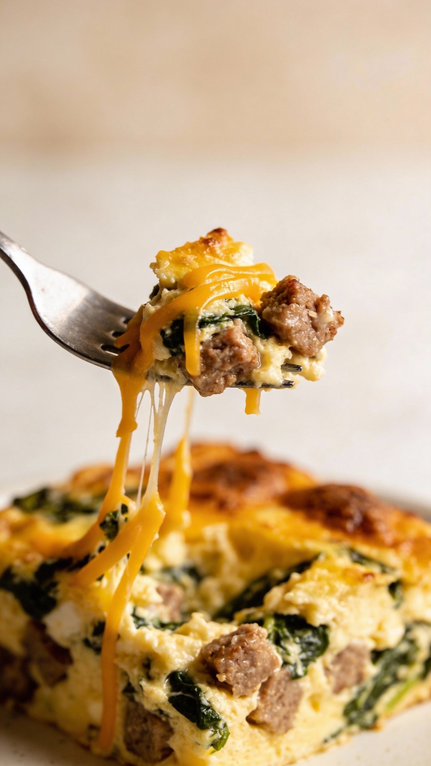forkful of sausage-spinach egg bake, melted cheddar strands