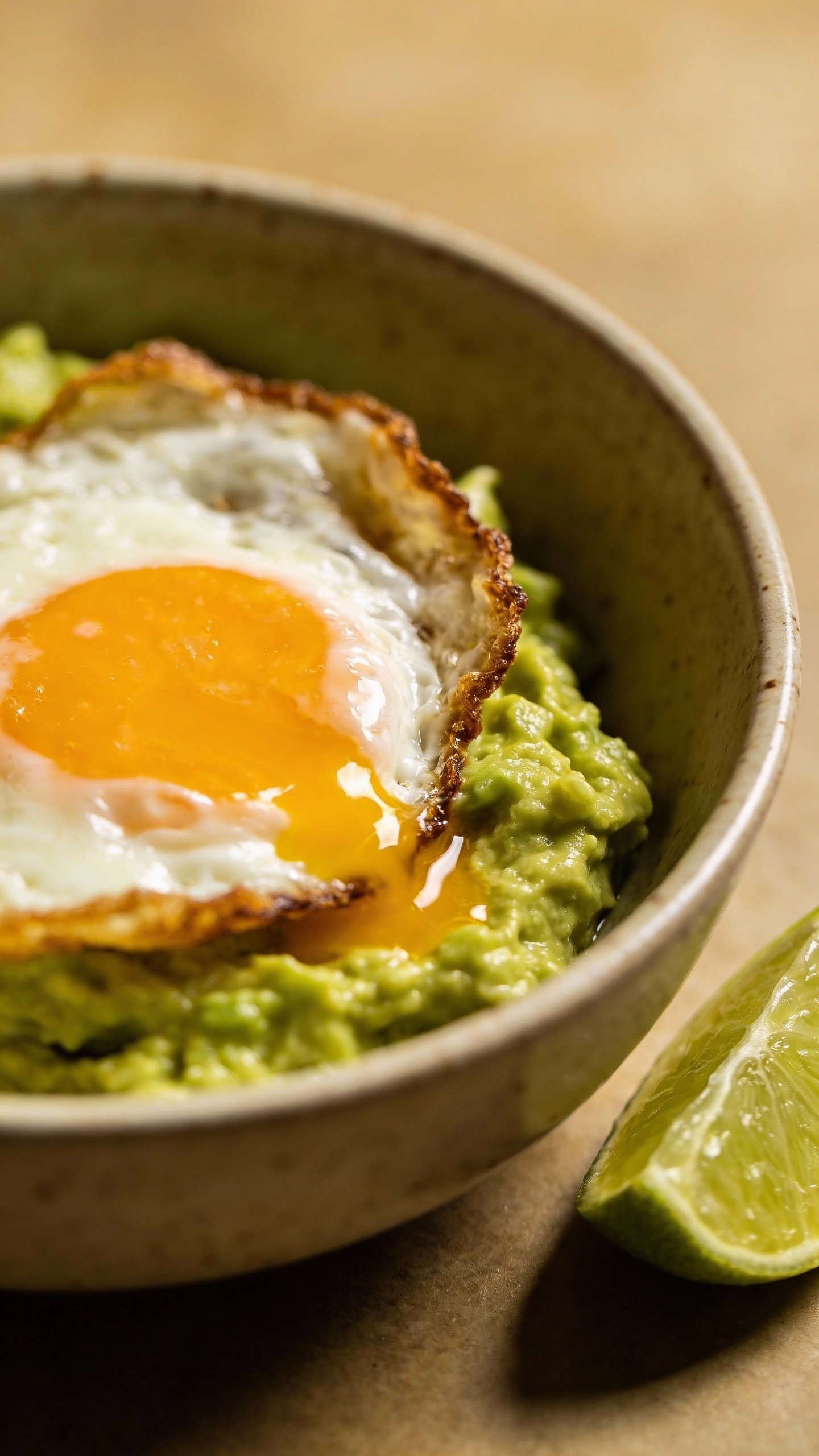 fried egg over mashed avocado in ceramic bowl, lime wedge