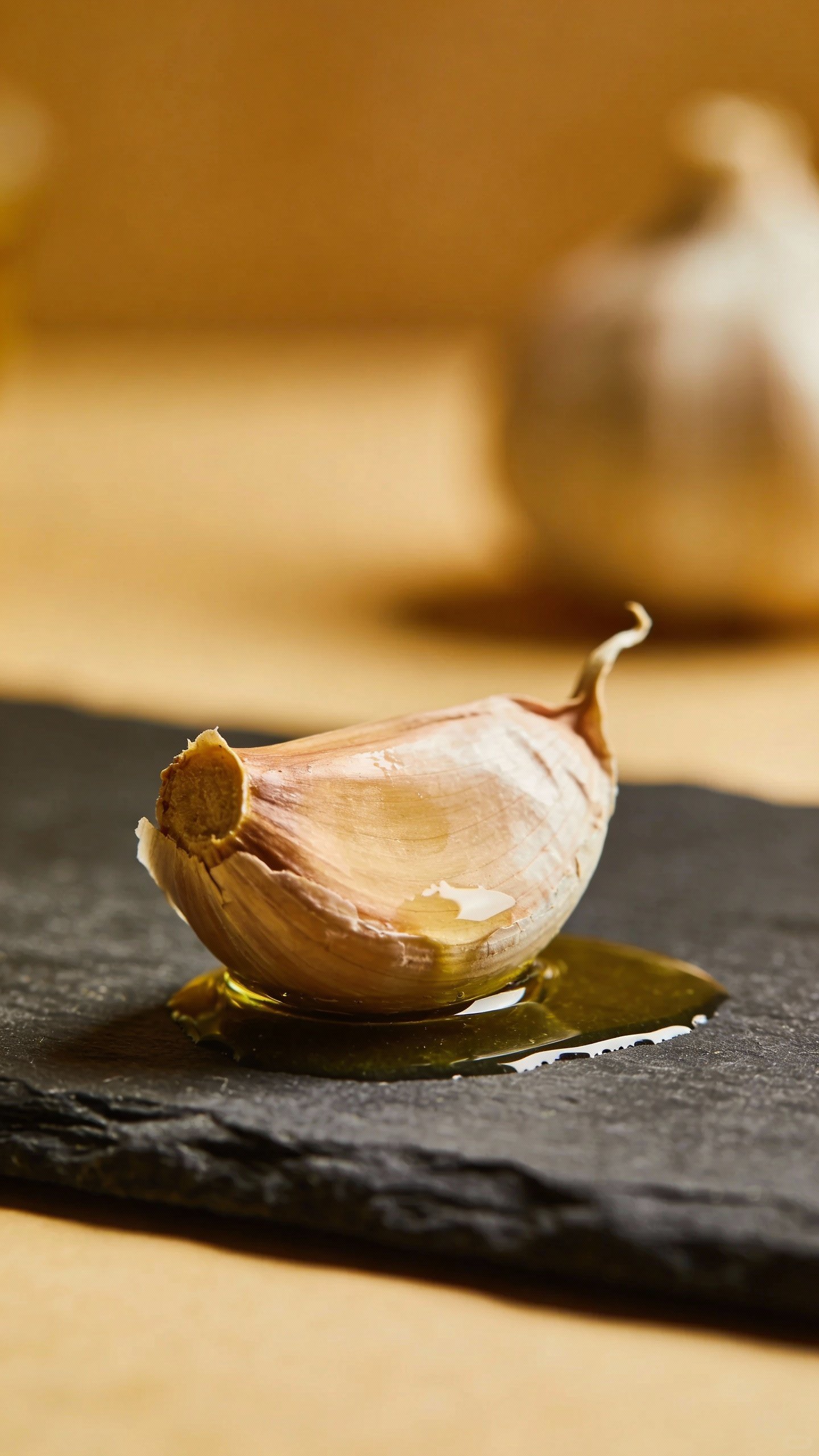 single garlic bulb on dark slate, olive oil sheen
