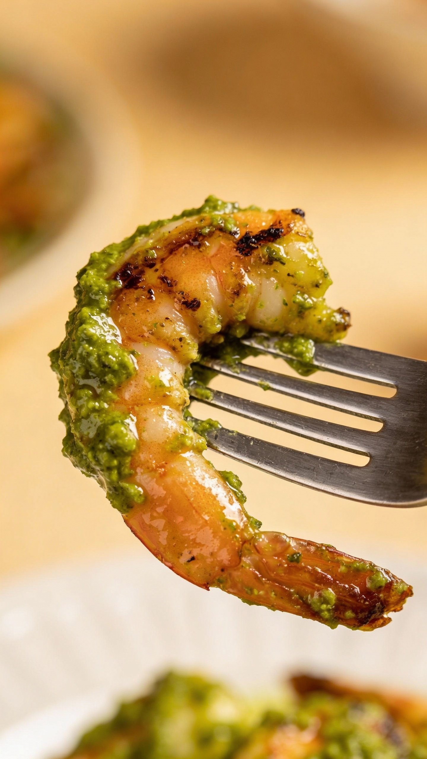 Single seared shrimp coated in pesto on fork