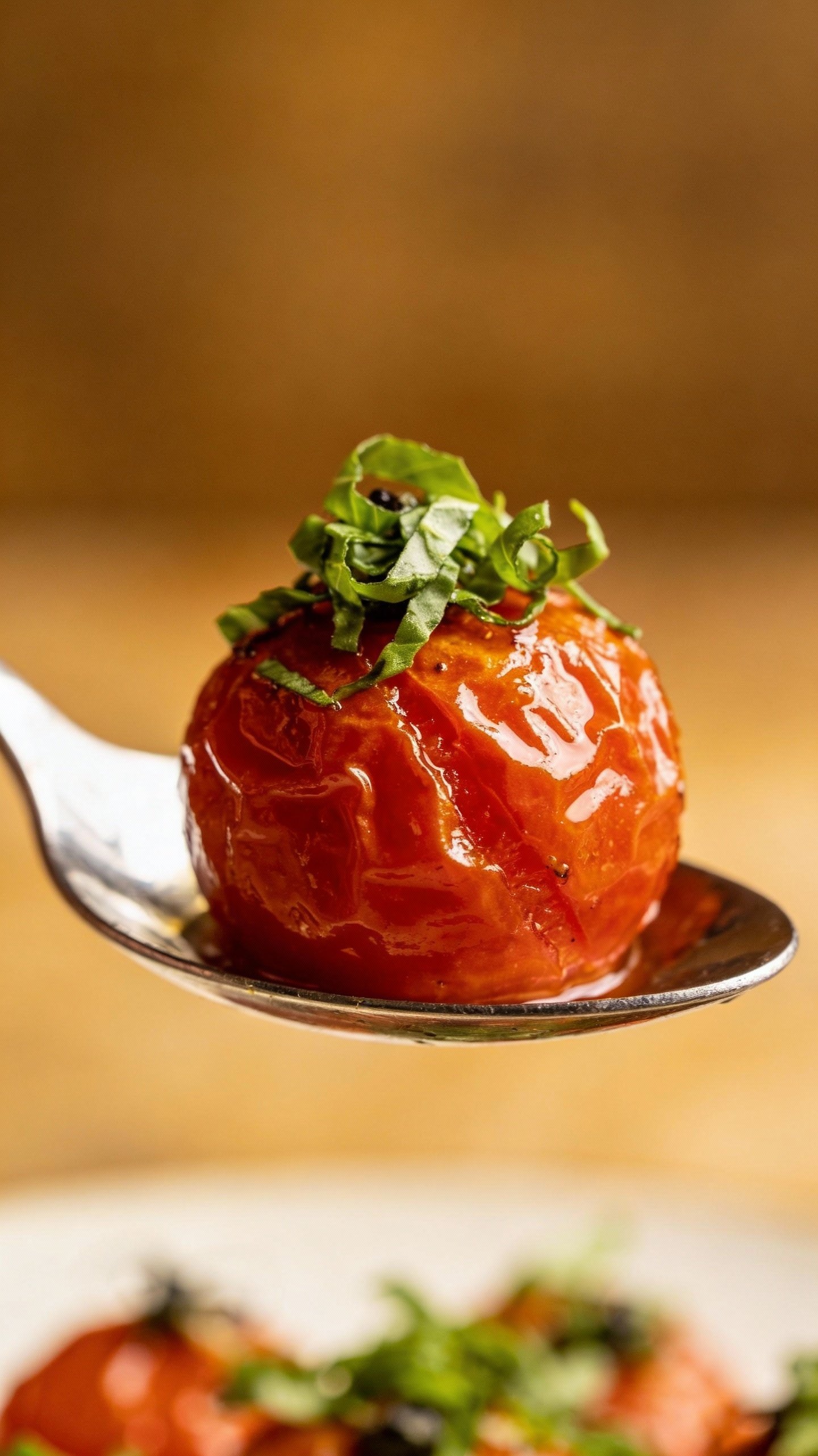 single glossy roasted tomato on spoon, basil chiffonade garnish
