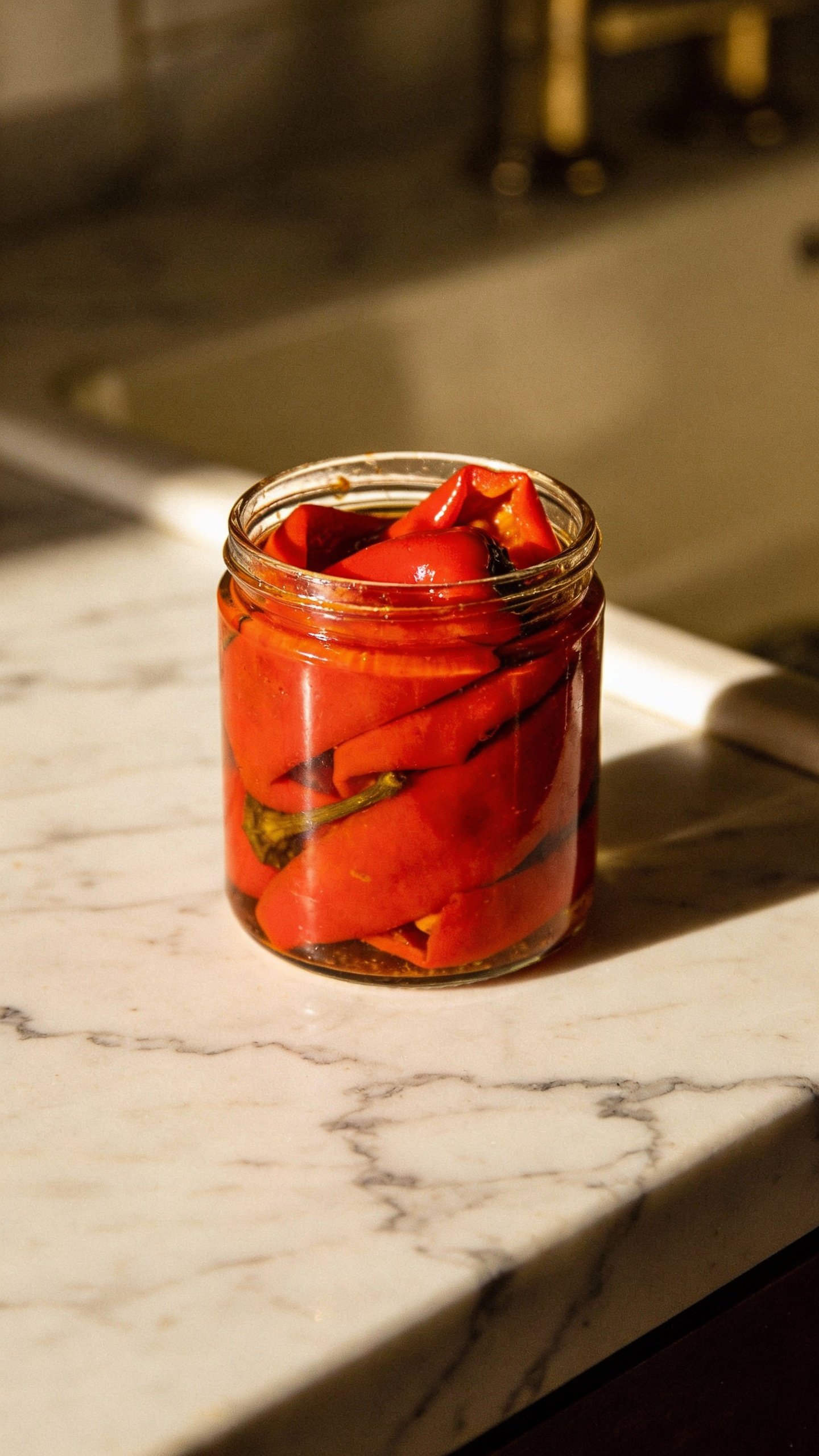 single jar of roasted red peppers on marble countertop