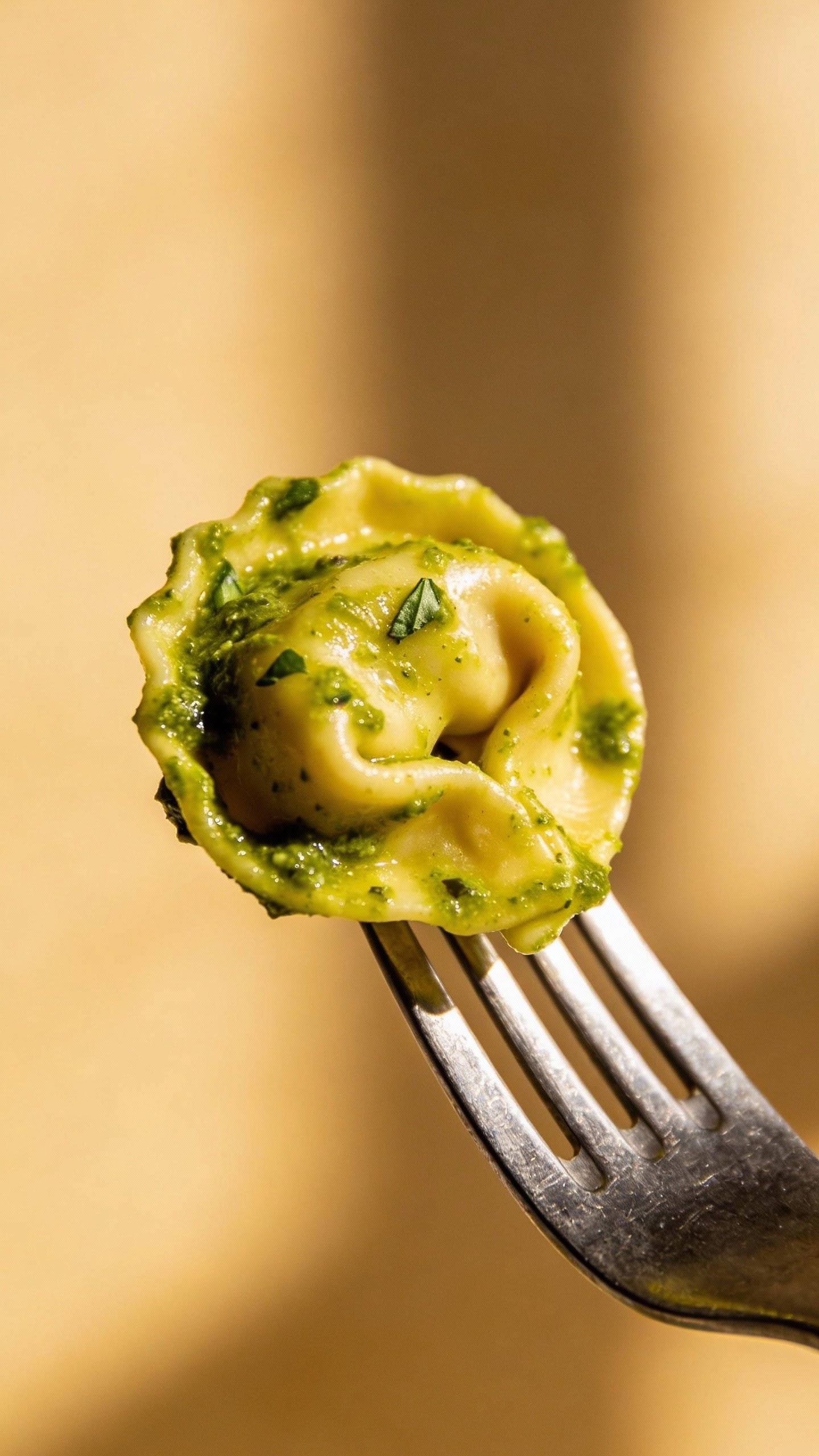 single cheese tortellini coated in green pesto on fork