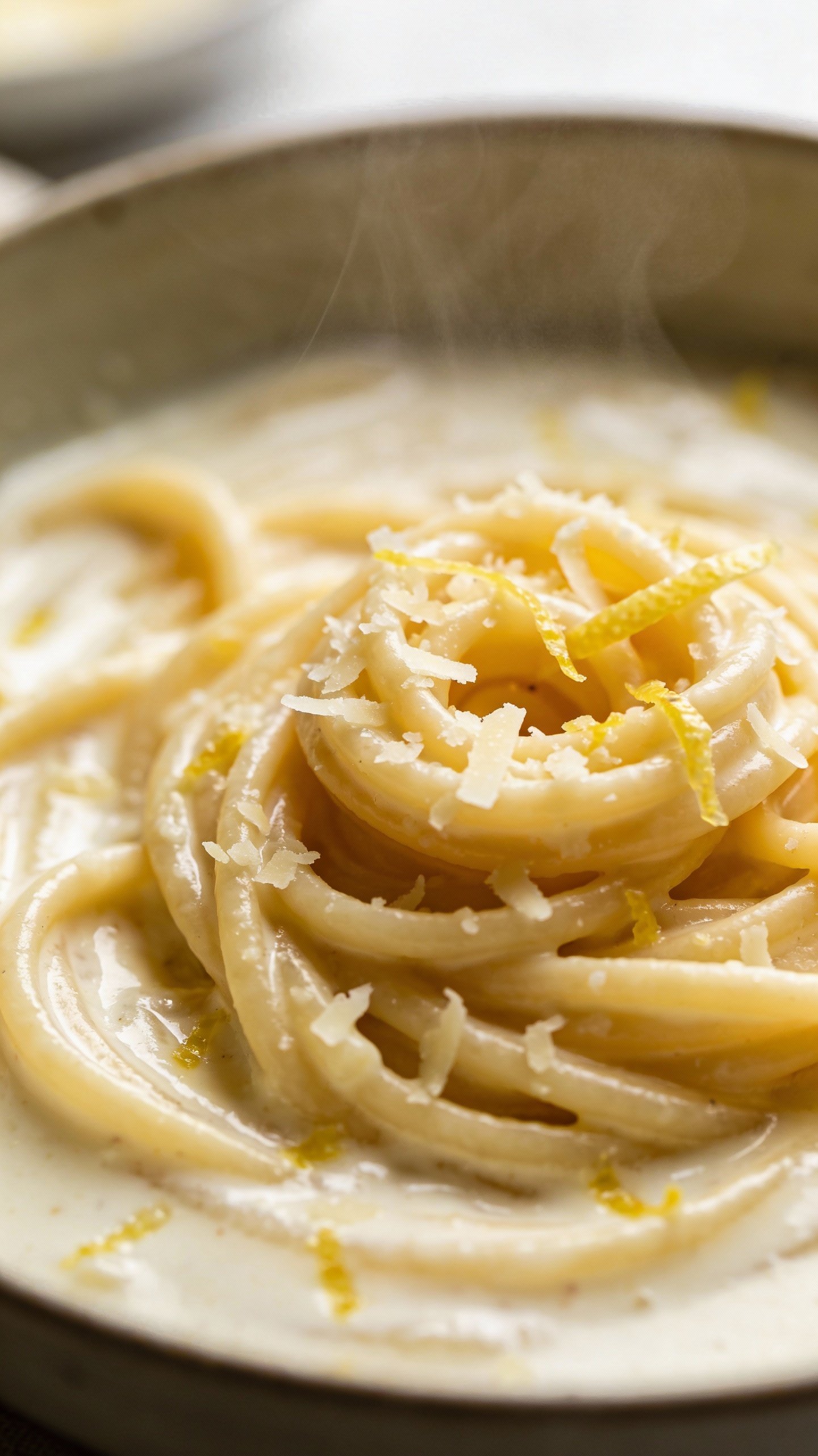 closeup bowl of creamy lemon parmesan pasta, twirled, steam rising