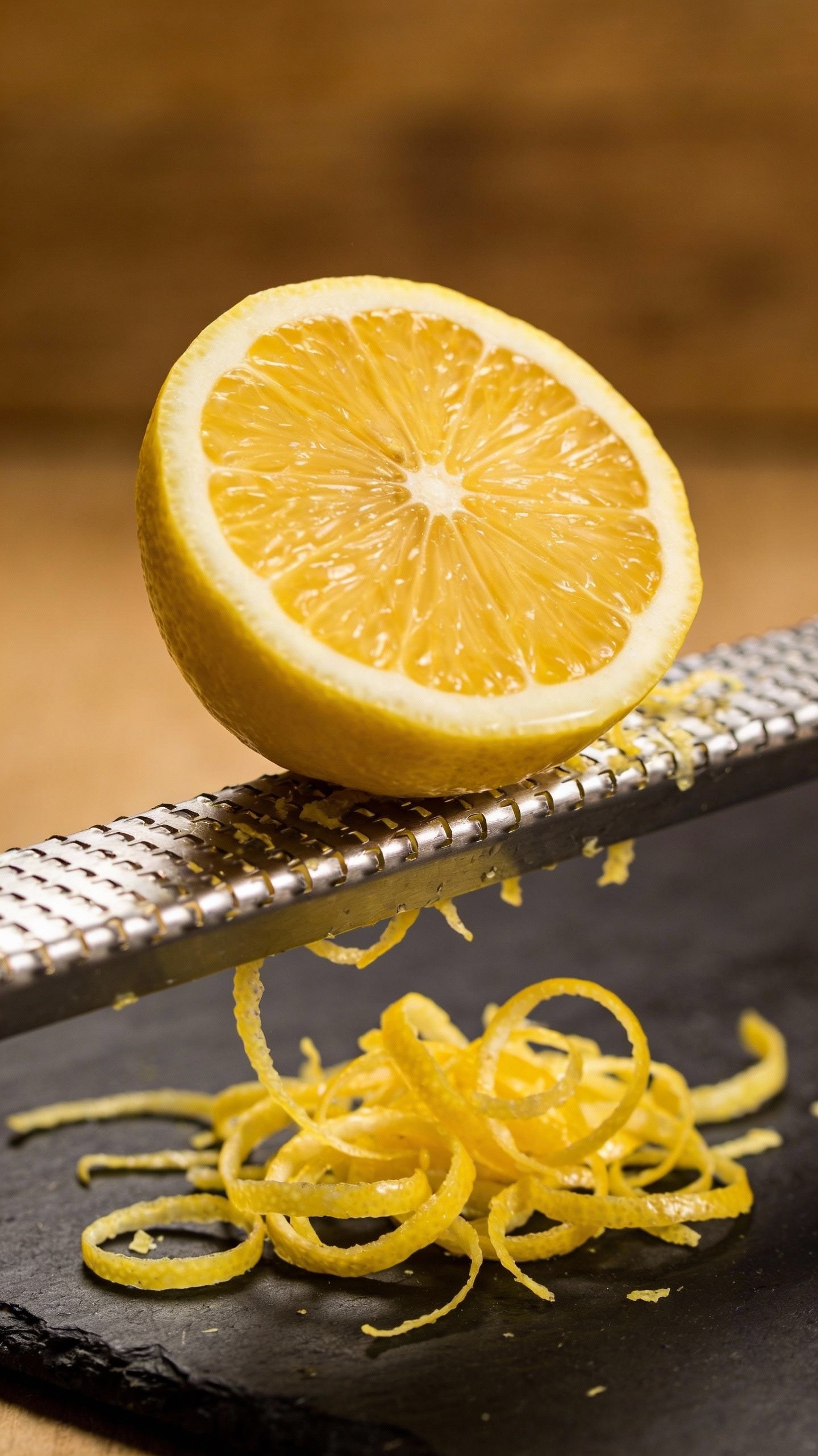 single lemon half zested on microplane, curls on black board