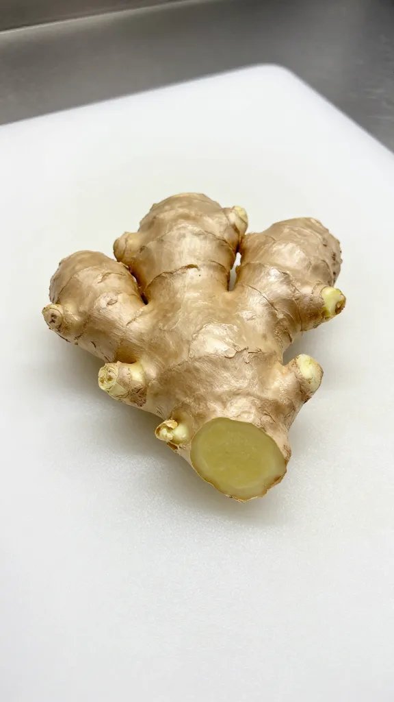 fresh ginger knob on white cutting board, sharp kitchen light