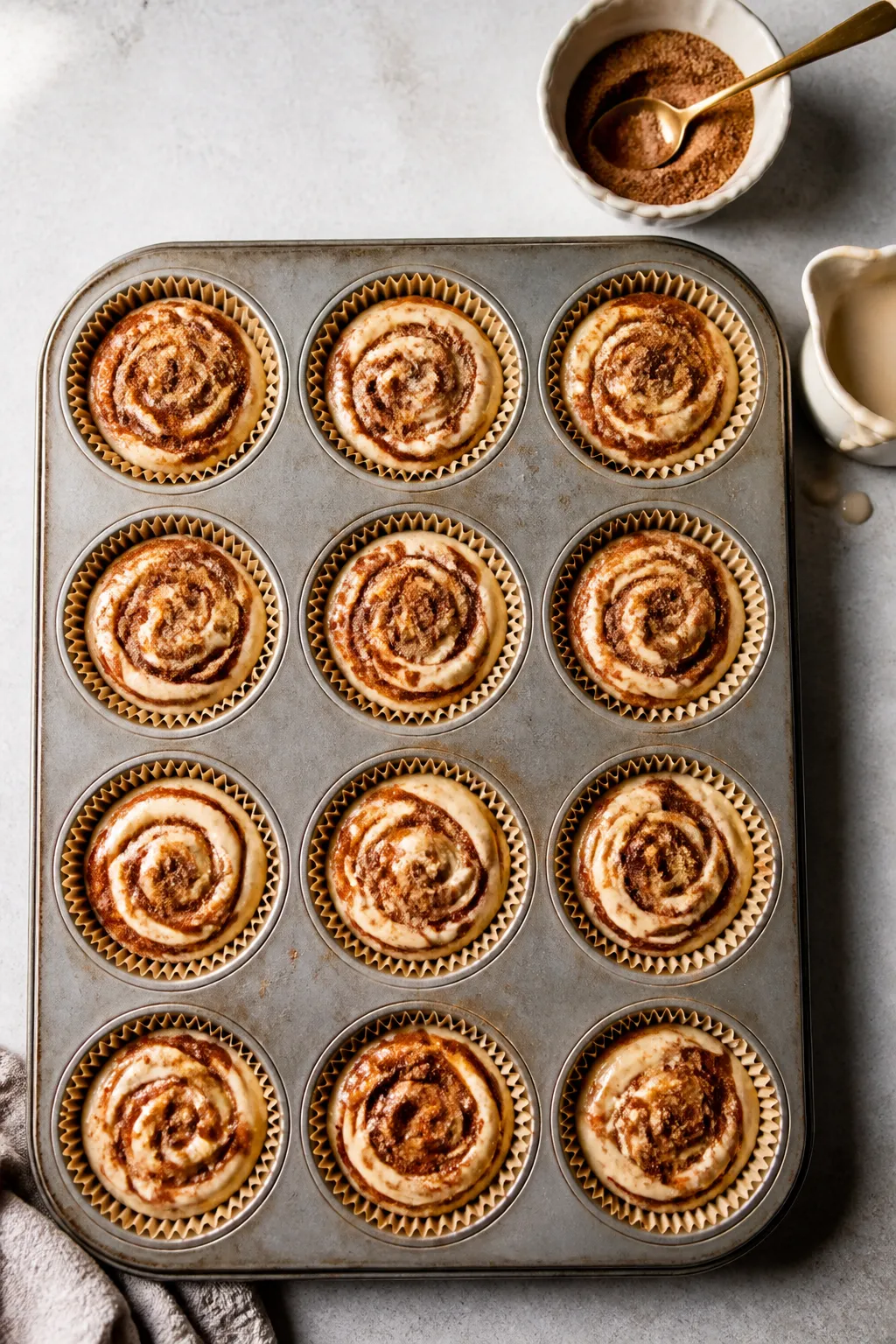 Overhead process shot of a muffin tin just filled and marbled: each lined cup 3/4 full with thick, s
