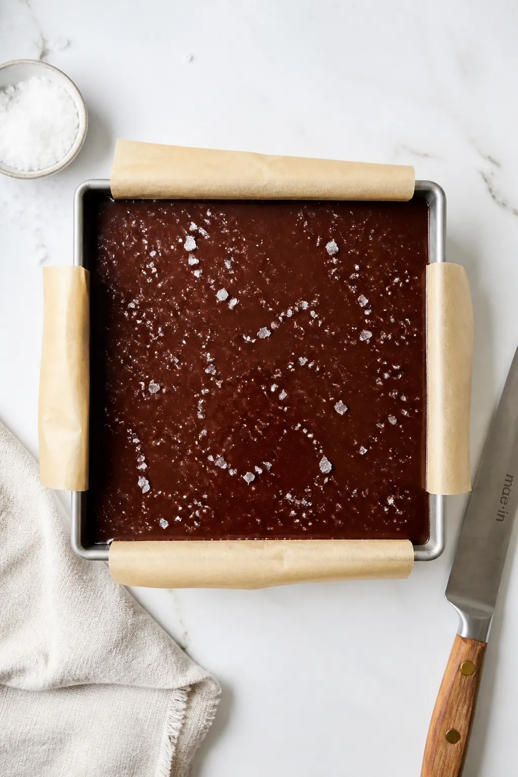 Overhead process shot of the slab in an 8x8 pan right after the melted dark chocolate has been poure